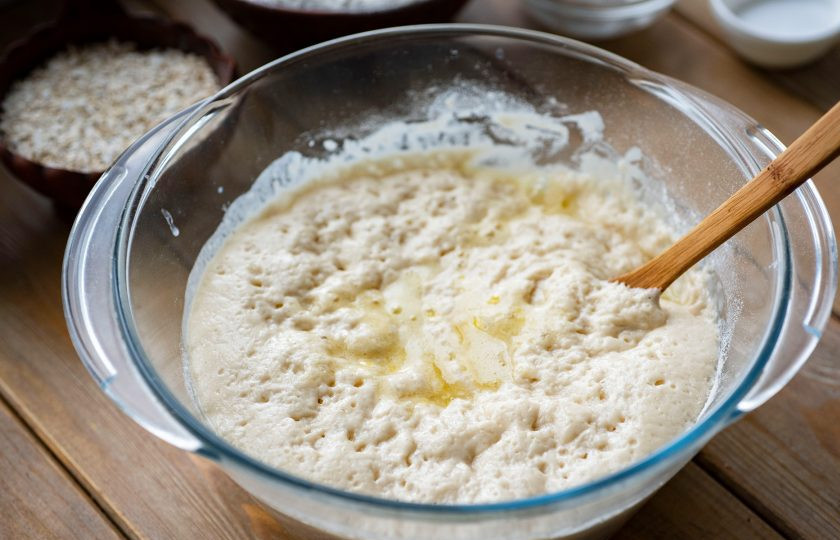 1. Этап. Булочки с овсяными хлопьями: Залейте к опаре сдобную смесь и перемешайте все ложкой.