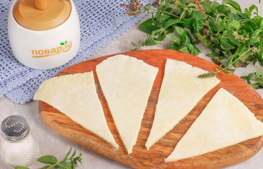 1. Этап. Творожные рогалики Нежнее нежного: Спустя указанное время извлеките тесто из холодильника и разделите его на две части. Подпылите мукой рабочую поверхность и раскатайте часть теста в округлый пласт. Нарежьте пласт на треугольные сегменты.