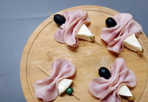 1. Этап. Мини-бутерброды Ассорти: Для 3 бутерброда взять шпажки. На шпажку нанизать отрезанный кусочек плавленого сыра. Затем нанизать 2 ломтика ветчины, сложенные гармошкой. Завершить композицию маслиной.