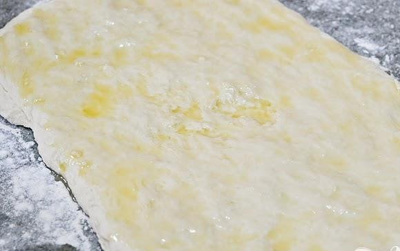 1. Этап. Булочки с корицей и пахтой: 4. Вылить 2 столовые ложки топленого масла на тесто и равномерно смазать его пальцами.