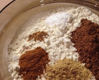 1. Этап. Рождественское имбирное печенье: Муку просейте через сито, добавьте ее к масляной смеси. Также высыпьте в миску какао-порошок, молотый сухой имбирь, корицу и мускатный орех.