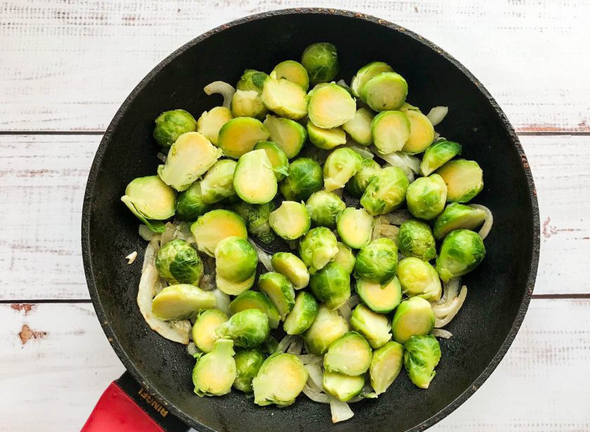 1. Этап. Тушеная брюссельская капуста с картошкой: Брюссельскую капусту нарежьте пополам, добавьте к луку и обжарьте в течение 5-7 минут.