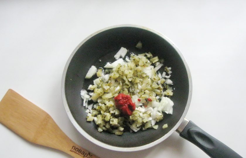 1. Этап. Солянка Ростовская: Выложите томатную пасту. Налейте несколько ложек куриного бульона в сковороду. Накройте её крышкой и тушите лук с соленым огурцом 12-15 минут.