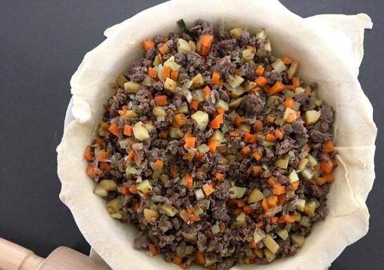 1. Этап. Пирог с мясом (вкусный): 2. Раскатайте тесто и разделите его на 2 части, выложите в форму одну часть и уложите внутрь начинку, посыпьте сыром.