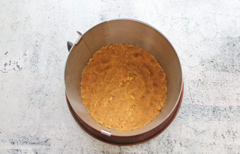 1. Этап. Банановый торт суфле: Раздвижное кольцо установите размером 22 сантиметра и установите на сервировочное блюдо. Переложите внутрь бисквитную крошку и утрамбуйте ровным слоем.