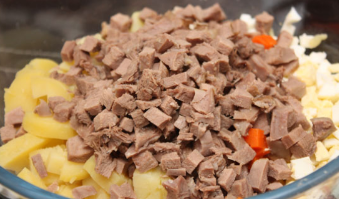 1. Этап. Салат Оливье с солеными огурцами: Сваренный говяжий язык режем мелкими кубиками и добавляем в салатницу.
