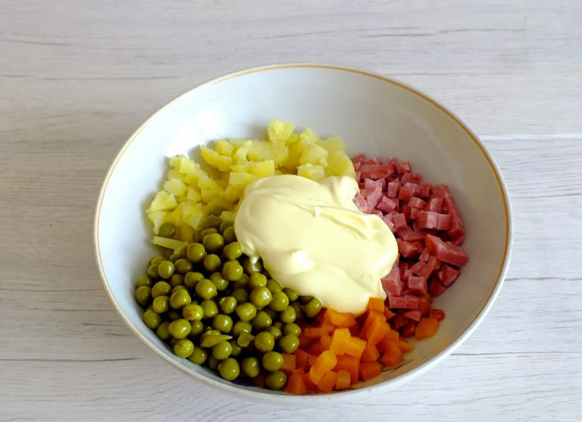 1. Этап. Салат Буковина: В салатник выложите подготовленные ингредиенты: картофель, морковь, колбасу. С горошка слейте жидкость и добавьте в салатник. Заправьте солью и майонезом. Перемешайте.