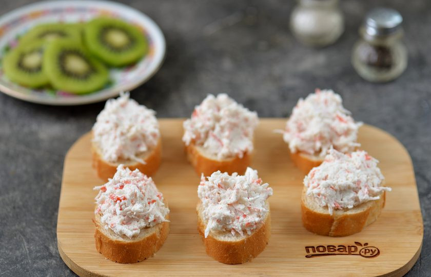 1. Этап. Бутерброды со сливочным сыром, киви и крабовыми палочками: Почистите от кожуры киви, нарежьте кружочками. На каждый ломтик хлеба выложите по полной чайной ложке приготовленной начинки.