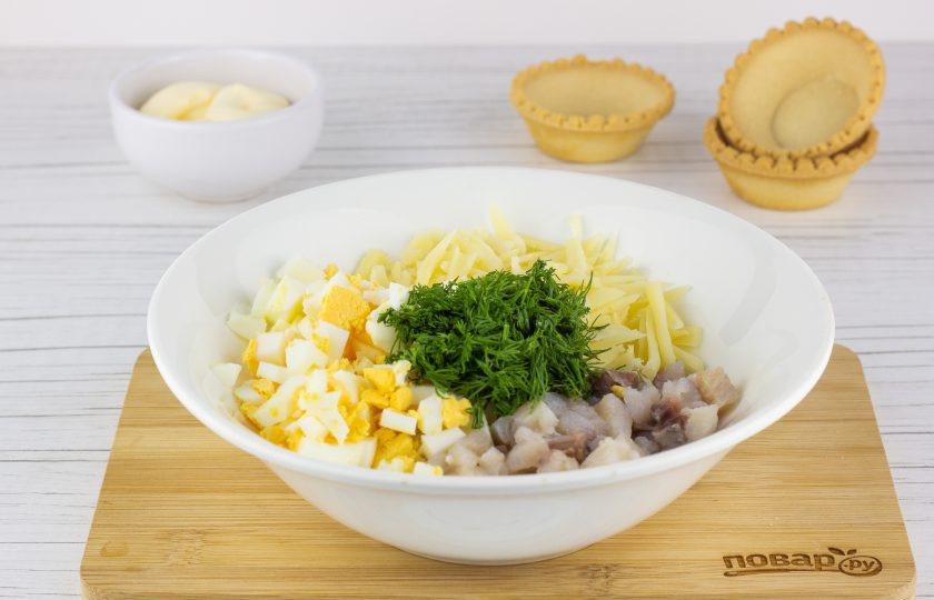 1. Этап. Закуска Тарталетки с сельдью на Новый год 2025: Небольшими кубиками нарежьте яйца и филе сельди. Сыр натрите на крупной терке, зелень порубите.
