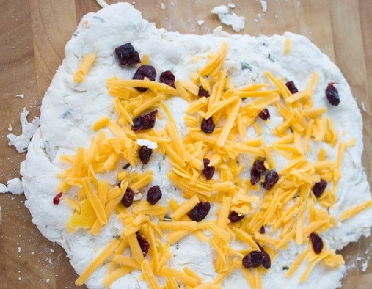 1. Этап. Сырное печенье с клюквой и розмарином: 3. Раскатайте тесто на присыпанной мукой поверхности. Соедините тертый сыр с клюквой. Присыпьте частью сыра тесто и аккуратно сверните.