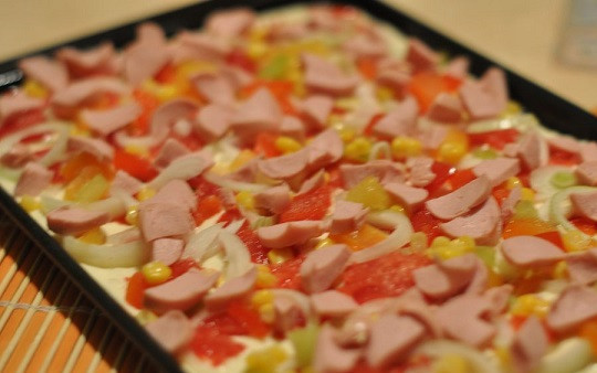 1. Этап. Быстрая пицца на кефире: 5. Противень или форму для запекания смажьте небольшим количеством масла или застелите пергаментом. Распределите тесто. Затем выложите немного соуса (идеальный вариант - это томатный соус с травами) и распределите ровным слоем начинку. Можно использовать колбасу, копчености, мясо, грибы или просто овощи, например.