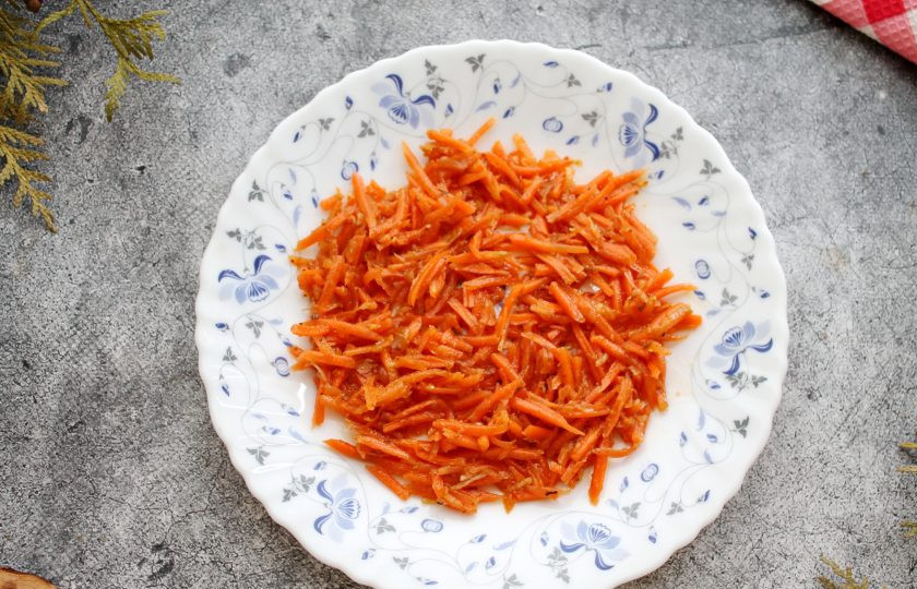 1. Этап. Салат Орхидея с чипсами и ветчиной: С моркови слейте жидкость и выложите ровным слоем на сервировочное блюдо. Если морковь длинная, порежьте ее на кусочки.