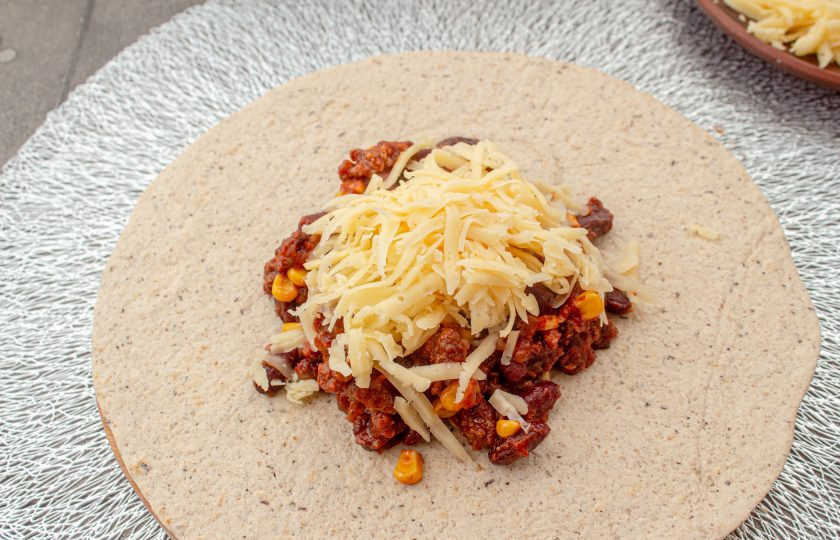 1. Этап. Буррито с фаршем и фасолью: Сыр натрите на терке. В центр лепешки выложите порцию фарша, сверху посыпьте сыром.