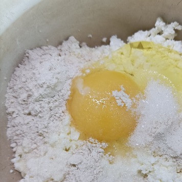 1. Этап. Сырники с апельсиновым соусом: Творог рассыпчатый не ниже 9% жирности выкладываем в посуду. Добавляем 1 яйцо, 1,5 ст. л. муки (цельнозерновая или белая). Добавляем сахар и крахмал. Перемешиваем ложкой до однородности.