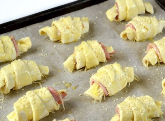 1. Этап. Круассаны с сыром и ветчиной: Выкладываем круассаны на противень, застеленный бумагой для выпечки. Смазываем верх взбитым яйцом и посыпаем семечками кунжута. Выпекаем 25-30 минут в нагретой до 180 градусов духовке.