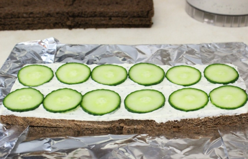 1. Этап. Торт с копченым лососем: Тонкими ломтиками нарежьте огурец и выложите поверх сливочного сыра.