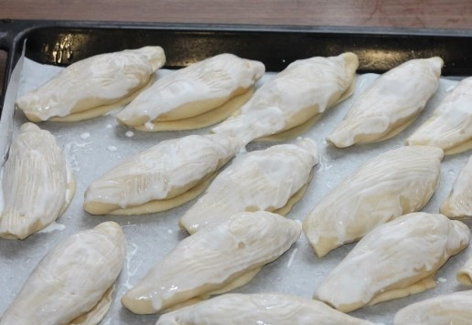 1. Этап. Пирожки из слоеного теста на кефире: 17. Формируем пирожки. Застилаем противень пекарской бумагой и смазываем маслом (растительным или холодным сливочным). Раскладываем заготовки пирожков и смазываем жидкой сметаной. Ставим противень в теплое место для расстойки пирожков, минут на 20.