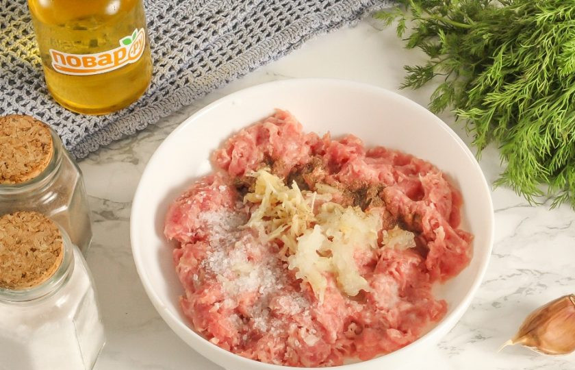 1. Этап. Балканские колбаски: Выложите мясной фарш в салатник или миску. Очистите лук и чеснок от кожуры, промойте в воде. Натрите на терке с мелкими ячейками половину луковицы и зубчики чеснока прямо в емкость. Всыпьте соль и молотый черный перец.