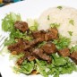 Говядина в пикантном соусе Продукты. Чеснок уже нарезан слайсами, мясо - кусочками. В миска готовим маринад из соевого соуса, коньяка, лимонного сока, растертого базилика, наломанного на кусочки жгучего перца, зерен розового перца, сахар и пару щепоток соли, хорошо перемешиваем до полного растворения соли и сахара. Выливаем в мясо, перемешиваем, и даем постоять под крышкой в холодильнике пару часов. Обжариваем чеснок на растительном масле до появления приятного запаха. Мясо, после маринования, отправляем в сковороду с чесноком вместе с жидкостью, слегка обжариваем минут 10. Добавляем 0,5 - 1 стакан говяжьего бульона (можно растворить в стакане воды часть бульонного кубика). И тушим под крышкой до готовности мяса. В конце, если требуется подсаливаем. Раскладываем в тарелки салатные листья, сверху мясо, в качестве гарнира - отварной рис.