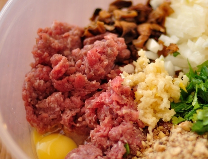 1. Этап. Тефтели с начинкой: В глубокой миске смешиваем говяжий фарш, измельченные чеснок (4 зубчика), грецкие орехи, зелень и грибы. Разбиваем куриное яйцо, солим и перчим, затем тщательно перемешиваем все ингредиенты до образования однородной массы.