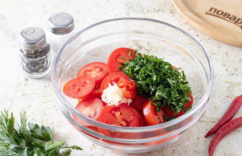 1. Этап. Острый салат из помидоров: Чеснок очистите и пропустите через пресс, острый перец чили порежьте кружочками, а зелень мелко порубите. Добавьте к помидорам.