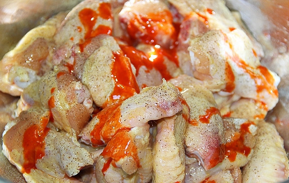 1. Этап. Острые крылья: 1. Куриные крылышки очищаем от перьев, моем и разрезаем на 3 части по сухожильям (самую маленькую не используем). Вытираем их бумажным полотенцем и перекладываем в миску, солим и перчим, добавляем подсолнечное масло, 10 миллилитров соуса чили, перемешиваем.