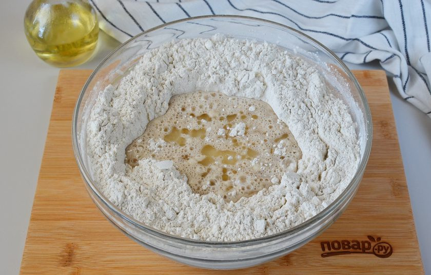 1. Этап. Черный хлеб простой: В центре сделайте лунку, перелейте дрожжевую смесь, добавьте растительное масло. Ложкой начните замес, потом перейдите на рабочий стол.