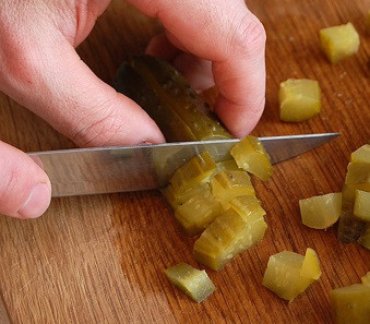 1. Этап. Тарталетки с селедкой: 6. Такие тарталетки с селедкой в домашних условиях - сплошная неожиданность. Еще один весьма непредсказуемый ингредиент - это маринованный огурчик. Его нужно нарезать кубиками.