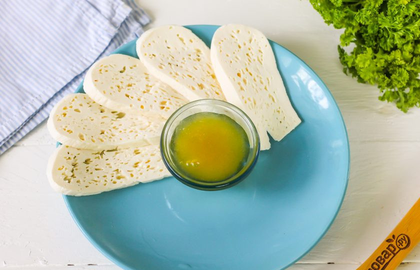 1. Этап. Сырная тарелка на Новый год: Выложите цветочный мед в округлую пиалу или креманку, разместите ее в середине тарелки. Извлеките брынзу из рассола, нарежьте ломтиками и дайте нарезке отдохнуть 5 минут на досочке, чтобы из нее вытек рассол. Затем выложите на тарелку.