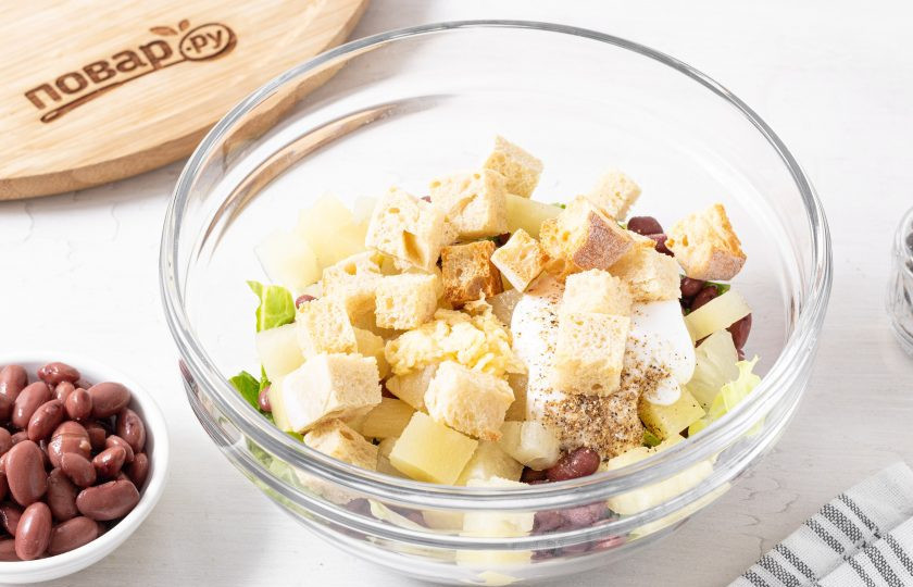 1. Этап. Салат с фасолью и ананасом: Посолите и поперчите. В конце добавьте сухарики.