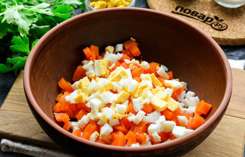 1. Этап. Салат Неженка с крабовыми палочками: Сваренную морковь нарежьте кубиками. Таким же образом нарежьте сваренные вкрутую куриные яйца. Добавьте эти ингредиенты в салат.