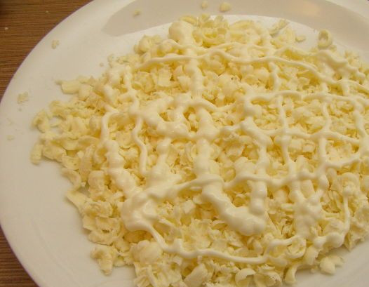 1. Этап. Крабовый салат с плавленым сыром: Выкладываем натертый сыр в салатник, смазываем его майонезом.