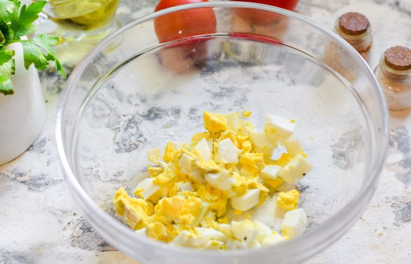 1. Этап. Салат Красная шапочка с помидорами: Куриное яйцо отварите вкрутую, почистите и нарежьте кубиками, переложите в салатник.