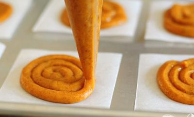 1. Этап. Тыквенные пирожные со сливочной начинкой: 4. Разрезать пергаментную бумагу на 24 квадрата по 7,5 см. Используя кондитерский мешок с круглым наконечником или большой пластиковый мешок с прорезью в одном угле, выдавить круги из теста на бумагу, начиная от середины и двигаясь по спирали наружу, около 5 см в диаметре.