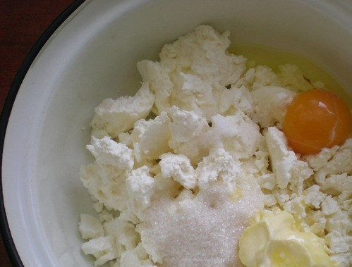 1. Этап. Бездрожжевое тесто с творогом: Достаньте из холодильника сливочное масло. Оно должно немного постоять при комнатной температуре и стать мягким. Поместите его в миску, всыпьте туда же творог, вбейте яйцо, добавьте сахар. Тщательно перемешайте ингредиенты до полной однородности.