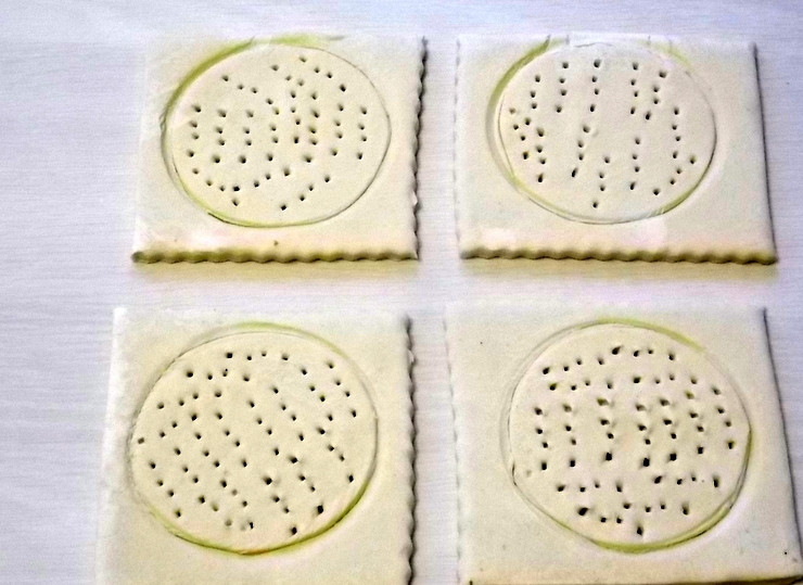 1. Этап. Яйца, запеченные с сыром: Немного раскатайте тесто. Разделите его на четыре части и наметьте круг на каждой. Проведите аккуратно ножом по контуру, не прорезая до конца. Сделайте частые проколы в круге.