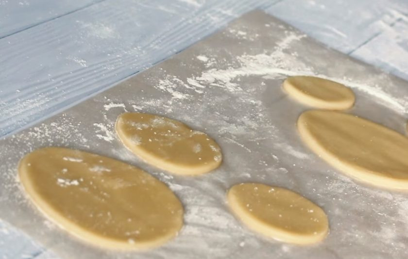 1. Этап. Пасхальное печенье в белковой глазури: 3. Тесто раскатайте в пласт 0,5 см на присыпанной мукой пергаментной бумаге и вырежьте разные по форме печенья. Сделайте в печенье отверстия с помощью вилки. Выпекайте его в разогретой до 180 градусов духовке 15 минут.