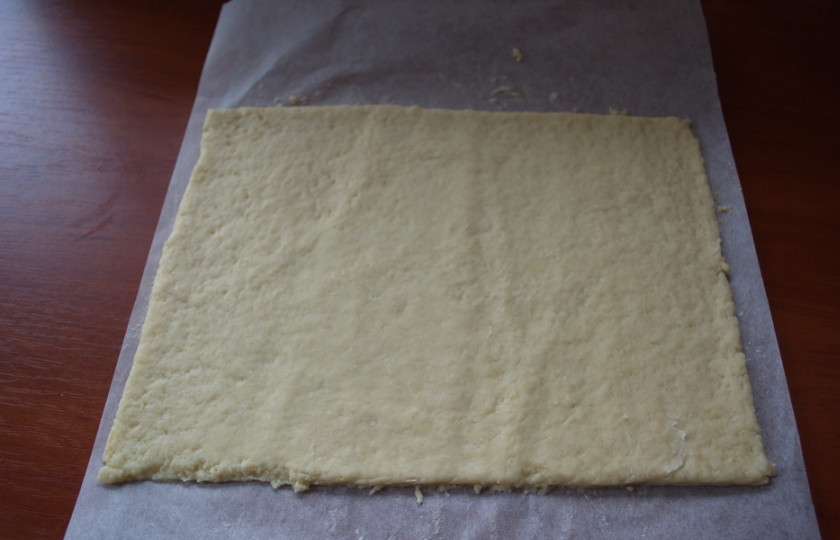 1. Этап. Печенье на кефире с вареньем: Одну часть теста раскатайте в пласт на бумаге для выпечки. Обрежьте ровно края.