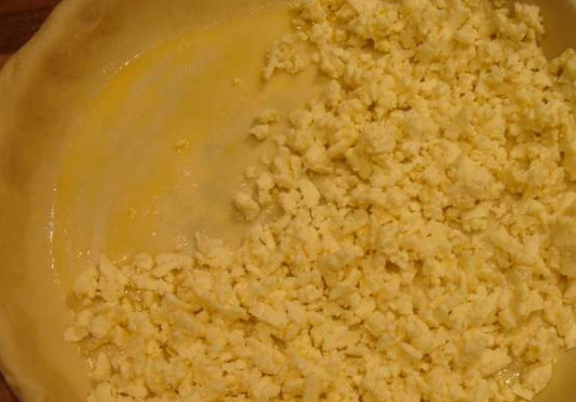 1. Этап. Ачма с сулугуни: Противень с высокими бортиками смажьте маслом. Большую часть теста раскатайте тонким слоем так, чтобы она была чуть больше его формы. Выложите тесто в противень таким образом, чтобы оно свисало с бортиков, смажьте его маслом, выложите на него 5-ю часть тертого сыра сулугуни.