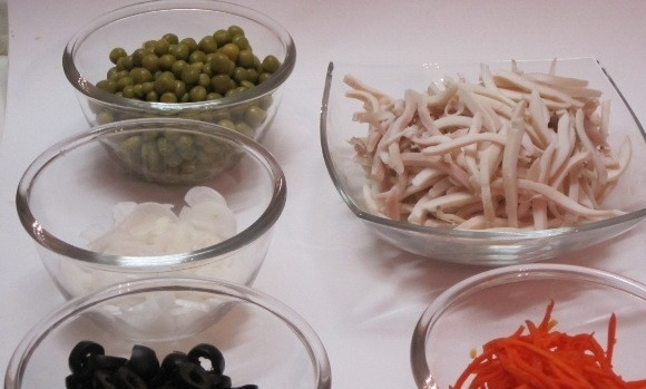 1. Этап. Салат Деликатесный: 3. Кальмары нарезаю тонкими полосками, луковицу очищаю и нарезаю полукольцами, консервированный горошек откидываю на сито, чтобы ушла вся вода, маслины без косточек нарезаю кольцами.