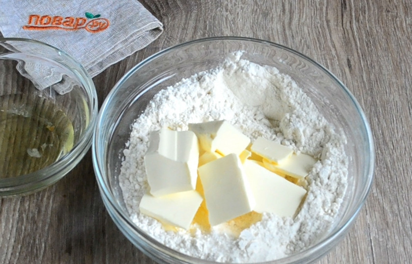 1. Этап. Новогоднее печенье Петушки: Туда положите 1 желток (белок поместите в чистую сухую пиалу, он нам понадобится для глазури), нарежьте небольшими кусочками охлажденное сливочное масло. Кстати, его можно также натереть на крупной терке, тогда будет легче и быстрее замешивать тесто.