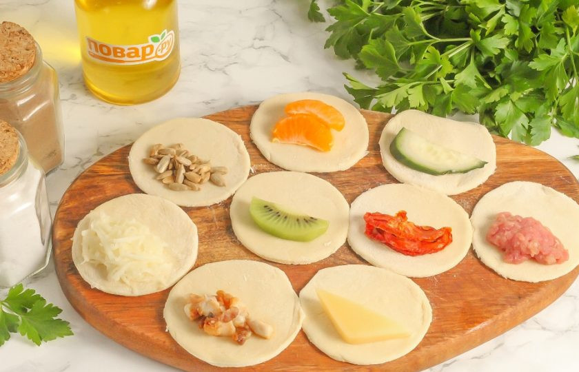 1. Этап. Вареники с сюрпризами на Старый Новый год: В это время подготовьте все продукты для начинок. Очистите их, если они в кожуре, все промойте. Разделите тесто на части и раскатайте одну из них в округлый пласт. С помощью чашки или стакана, обмакнутого в муку, вырежьте круги из теста. На каждый из них выложите начинку: семечки, тертый картофель, дольки мандарина, киви, огурца, вяленые томаты и т.д.