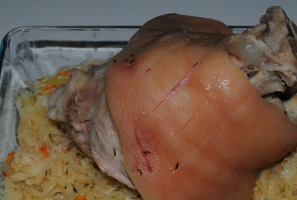 1. Этап. Свиная рулька по-немецки: В форму для выпечки уложите слой капусты с луком. Сверху положите рульку. Обмажьте её чесноком и медовой смесью.