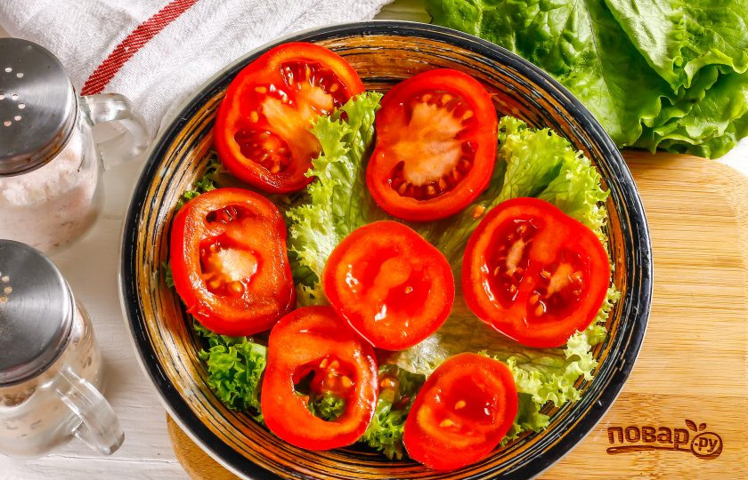 1. Этап. Салат с икрой минтая: Промойте помидор в воде, нарежьте его кольцами, вырезая черенок. Выложите нарезку на листья салата.