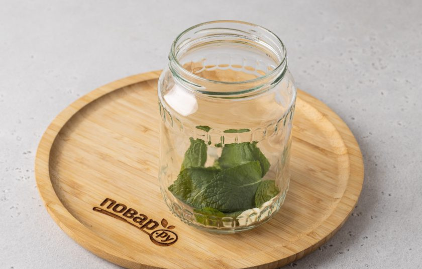 1. Этап. Огурцы с мятой на зиму: На дно чистой стерилизованной банки выложите очищенный чеснок и листья мяты.