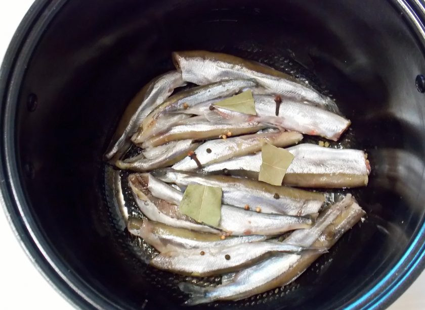 1. Этап. Домашние шпроты в мультиварке: Чашу мультиварки смажьте растительным маслом и выложите рыбу. Добавьте лавровый лист, перец и гвоздику.