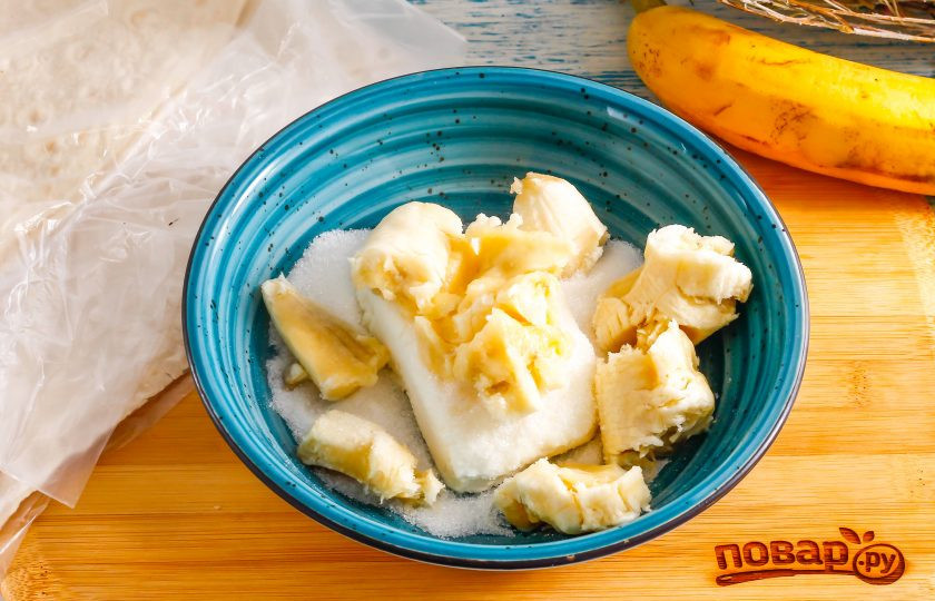 1. Этап. Конвертики из лаваша с творогом и бананом: В глубокую емкость выложите творог, всыпьте сахар. Очистите банан от кожуры и разломите на части, добавьте в емкость. По желанию всыпьте ванильный сахар или другой ароматизатор. Тщательно помните и перемешайте начинку.