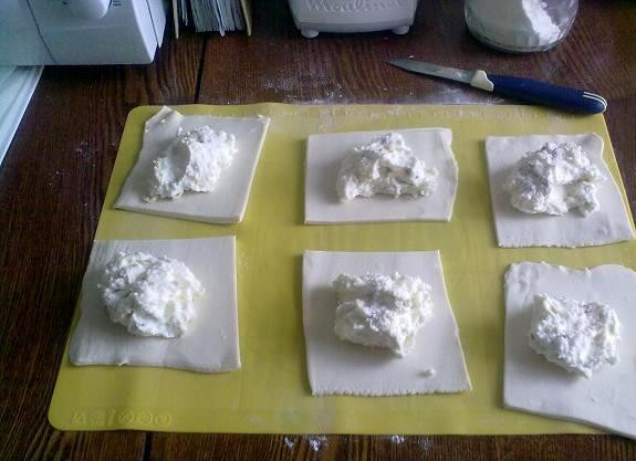 1. Этап. Булочки из слоеного теста с творогом: Тесто предварительно разморозьте, раскатайте и поделите на 10-12 квадратных частей. В центр каждого квадратика выложите начинку.