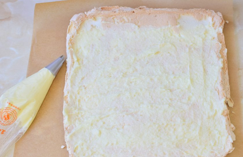 1. Этап. Меренговый рулет с заварным кремом: Немного крема отложите в кондитерский мешок для декора. Оставшийся крем распределите по меренге, немного не доходя до краев.