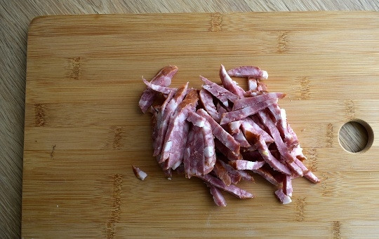 1. Этап. Салат Иришка с сухариками: Снимите с колбасы оболочку, нарежьте брусочками.